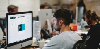 man in gray sweatshirt sitting on chair in front of iMac