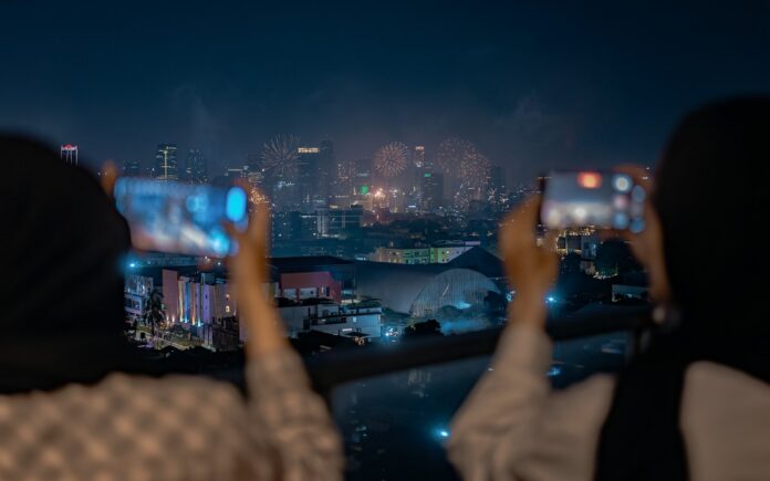 Photo by Alim Two people taking pictures of a city at night